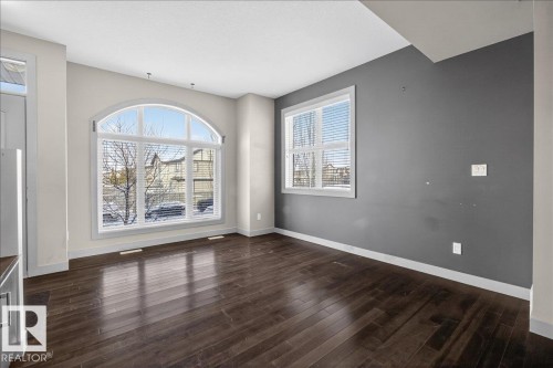 Spacious interior featuring dark hardwood flooring, an arched window, and a secondary rectangular window, providing ample natural light - 2105 Casselman Link Link, Edmonton, AB - Indoor Photo Showing Other Room
