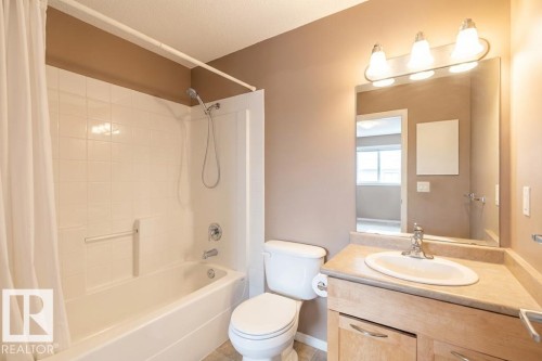 The bathroom features a bathtub with a shower, a toilet, and a vanity with a sink and storage cabinetry below - 1-204 4245 139 Avenue, Edmonton, AB - Indoor Photo Showing Bathroom