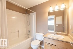 The bathroom features a bathtub with a shower, a toilet, and a vanity with a sink and storage cabinetry below - 