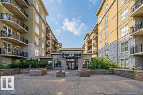 The property features a multi-story building with balconies, stone facade elements, and well-maintained landscaping with planters and shrubs - 1-204 4245 139 Avenue, Edmonton, AB - Outdoor With Balcony