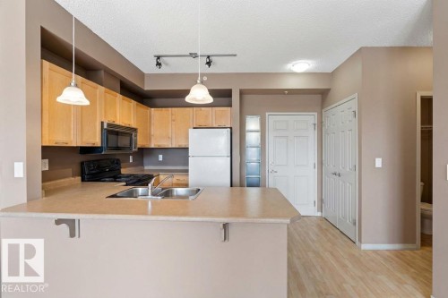 The kitchen features light wood cabinetry, a double basin sink, and pendant lighting - 1-204 4245 139 Avenue, Edmonton, AB - Indoor Photo Showing Kitchen With Double Sink