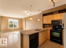 This open concept living space features a kitchen with light wood cabinetry, a double basin sink, and black appliances, including a microwave, oven, and dishwasher - 1-204 4245 139 Avenue, Edmonton, AB  - Indoor Photo Showing Kitchen With Double Sink 