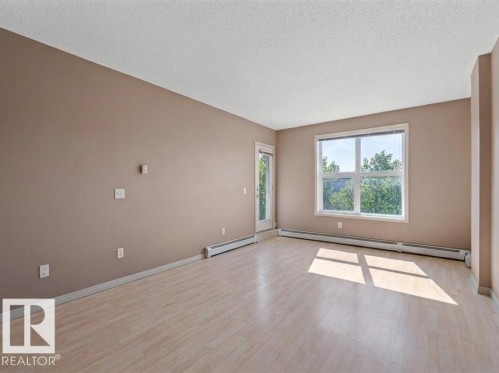 This room features light-colored flooring, neutral-toned walls, and a window that provides natural light and a view of trees - 1-204 4245 139 Avenue, Edmonton, AB - Indoor Photo Showing Other Room