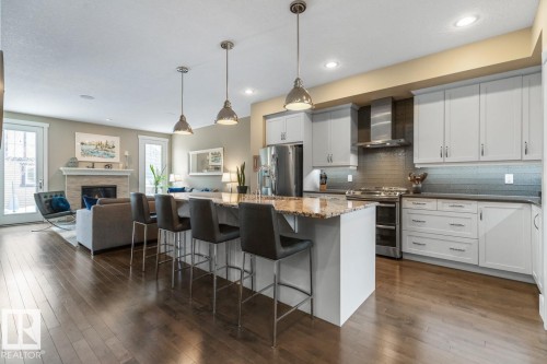 Open Concept Kitchen with Upgraded Granite Island Countertop, Gas Stove, Built in Microwave, Bar Space, Upgraded Cabinets (including Pots and Pans Drawers), and Maple Hardwood Flooring - 7432 Colonel Mewburn Road, Edmonton, AB - Indoor Photo Showing Kitchen With Upgraded Kitchen