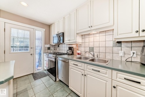 The kitchen features white cabinetry, stainless steel appliances, a double basin sink, and tiled flooring - 597 Millbourne Road E, Edmonton, AB - Indoor Photo Showing Kitchen With Double Sink