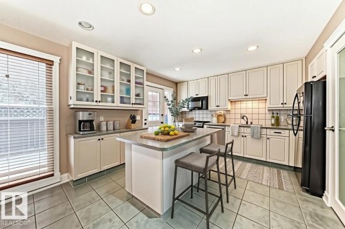 The kitchen features a central island with countertop seating, extensive cabinetry with both solid and glass-front doors, and tile flooring - 597 Millbourne Road E, Edmonton, AB - Indoor Photo Showing Kitchen With Upgraded Kitchen