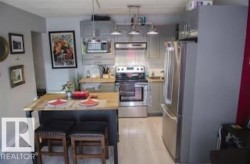 Kitchen with appliances with stainless steel finishes, light wood finished floors, a breakfast bar, range hood, and hanging light fixtures - 