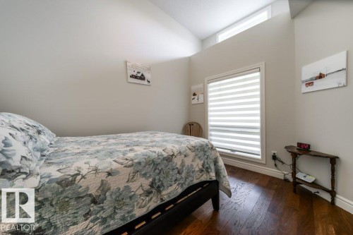 This room features rich hardwood flooring, a window with horizontal blinds, and vaulted ceilings - 3 8050 Orchards Green, Edmonton, AB - Indoor Photo Showing Bedroom