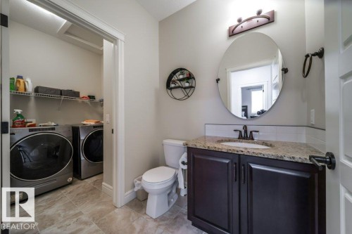 The property features a bathroom with a dark wood vanity, a granite countertop, and a round mirror - 3 8050 Orchards Green, Edmonton, AB - Indoor Photo Showing Laundry Room