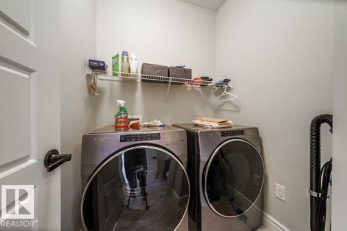 Dedicated laundry space featuring a modern washer and dryer set, and wall-mounted shelving for storage - 3 8050 Orchards Green, Edmonton, AB - Indoor Photo Showing Laundry Room