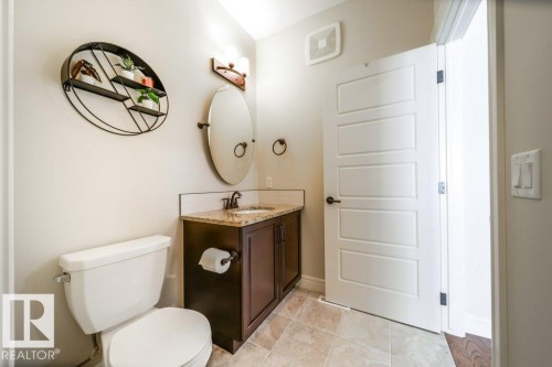 This functional bathroom features a toilet, a vanity with a granite countertop, and a white paneled door - 3 8050 Orchards Green, Edmonton, AB - Indoor Photo Showing Bathroom