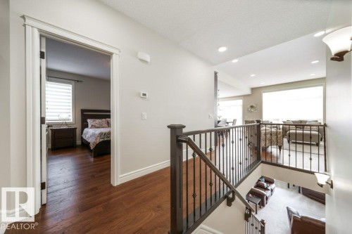 The interior features hardwood flooring, a staircase with dark wood handrails and wrought iron balusters, and recessed lighting - 3 8050 Orchards Green, Edmonton, AB - Indoor Photo Showing Other Room
