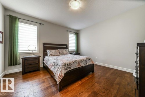 This room features hardwood flooring, light-colored walls, and two windows with blinds and drapes - 3 8050 Orchards Green, Edmonton, AB - Indoor Photo Showing Bedroom