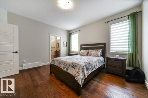 This space features rich hardwood floors and two windows with blinds and green drapes, offering natural light - 3 8050 Orchards Green, Edmonton, AB - Indoor Photo Showing Bedroom