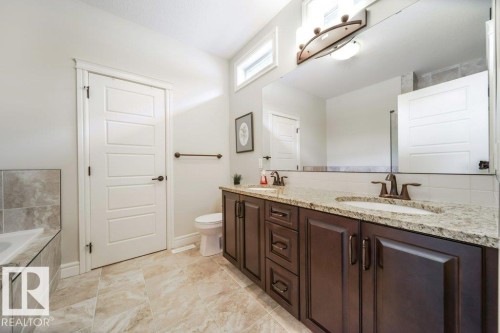 Bathroom featuring a double vanity with dark wood cabinetry and granite countertops, a large mirror, and tiled flooring - 3 8050 Orchards Green, Edmonton, AB - Indoor Photo Showing Bathroom