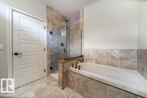 The bathroom features a built-in bathtub, a walk-in shower with a glass enclosure, and tiled walls and flooring - 3 8050 Orchards Green, Edmonton, AB - Indoor Photo Showing Bathroom