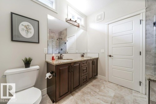 Bathroom featuring a dual vanity with granite countertops, dark wood cabinetry, a large mirror, and tiled flooring - 3 8050 Orchards Green, Edmonton, AB - Indoor Photo Showing Bathroom