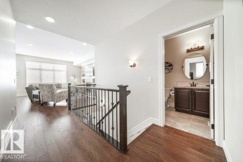 This property features rich hardwood flooring throughout the main hallway, leading to a bright living area with a large window - 3 8050 Orchards Green, Edmonton, AB - Indoor Photo Showing Other Room