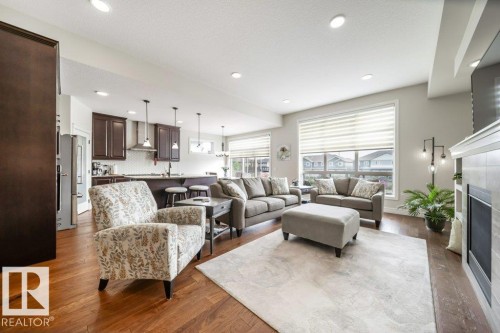 Bright and spacious open-concept living area featuring rich hardwood floors, a modern fireplace, and recessed lighting - 3 8050 Orchards Green, Edmonton, AB - Indoor Photo Showing Living Room With Fireplace