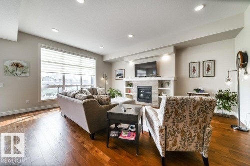Living room featuring hardwood flooring, a large window with blinds, and recessed lighting - 3 8050 Orchards Green, Edmonton, AB - Indoor Photo Showing Living Room With Fireplace