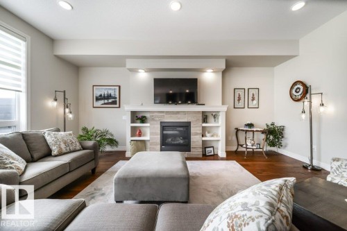 The living room features hardwood flooring, a fireplace with a stone surround, and recessed lighting - 3 8050 Orchards Green, Edmonton, AB - Indoor Photo Showing Living Room With Fireplace