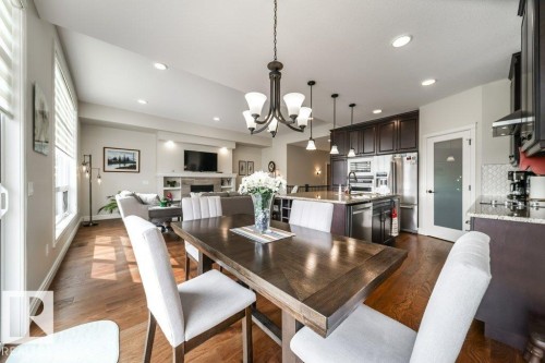 This property features an open-concept living area with hardwood flooring, a dining area with a chandelier, and a kitchen with dark cabinetry, granite countertops, and stainless steel appliances - 3 8050 Orchards Green, Edmonton, AB - Indoor Photo Showing Dining Room