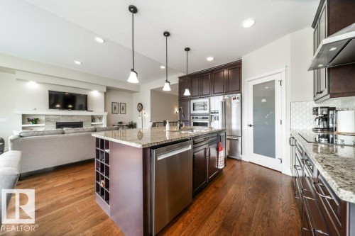 The kitchen features a large island with a granite countertop, pendant lighting, and stainless steel appliances, including a dishwasher and refrigerator - 3 8050 Orchards Green, Edmonton, AB - Indoor Photo Showing Kitchen With Upgraded Kitchen