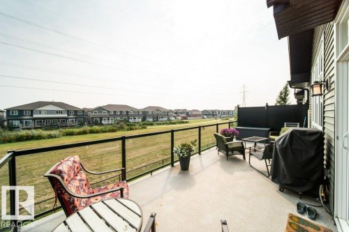The property features an expansive outdoor patio with a glass railing, providing views of a grassy field and distant residences - 3 8050 Orchards Green, Edmonton, AB - Outdoor With Deck Patio Veranda With Exterior
