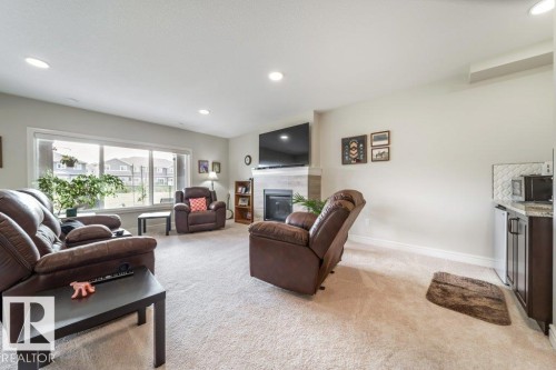 Living area featuring carpeted floors, a large window, and a fireplace with a mantel - 3 8050 Orchards Green, Edmonton, AB - Indoor Photo Showing Living Room With Fireplace