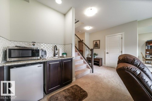 The property features a functional wet bar with a stainless steel microwave, a compact refrigerator, a sink, and dark wood cabinetry - 3 8050 Orchards Green, Edmonton, AB - Indoor