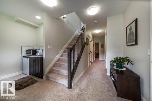 This inviting interior features a carpeted staircase with a dark wood and wrought iron railing, leading to an upper level - 3 8050 Orchards Green, Edmonton, AB - Indoor Photo Showing Other Room