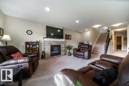 This living area features a fireplace with a stone surround, recessed lighting, and carpeted flooring - 3 8050 Orchards Green, Edmonton, AB - Indoor Photo Showing Living Room With Fireplace