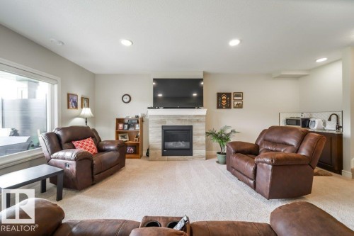 Living area featuring a fireplace with a light-colored tile surround, recessed lighting, and a window - 3 8050 Orchards Green, Edmonton, AB - Indoor Photo Showing Living Room With Fireplace