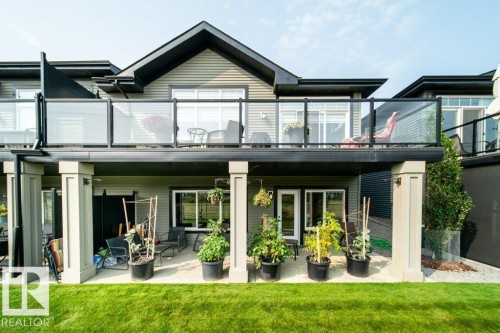 The property features a large yard with a lawn, a ground level patio, and a balcony with glass railings - 3 8050 Orchards Green, Edmonton, AB - Outdoor With Deck Patio Veranda