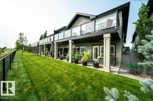The property features a well-maintained lawn with a chain-link fence bordering an open field - 3 8050 Orchards Green, Edmonton, AB - Outdoor With Deck Patio Veranda