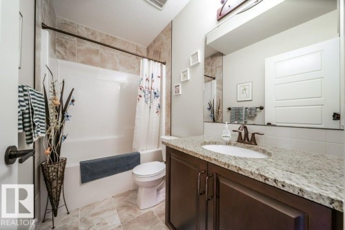 This bathroom features a vanity with a granite countertop and an integrated sink, a large mirror, and a shower-tub combination with tiled walls - 3 8050 Orchards Green, Edmonton, AB - Indoor Photo Showing Bathroom