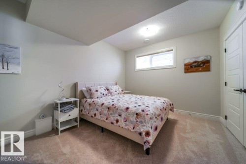 This room features light-colored carpeting, a window with blinds, and a white paneled door with dark hardware - 3 8050 Orchards Green, Edmonton, AB - Indoor Photo Showing Bedroom