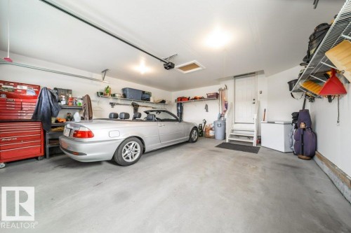 Spacious garage featuring concrete flooring, overhead lighting, an overhead door track system, and wall-mounted shelving for storage - 3 8050 Orchards Green, Edmonton, AB - Indoor Photo Showing Garage