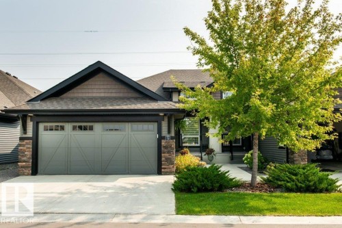The property features an attached garage with a light gray door and decorative window inserts, complemented by stone accents on the facade - 3 8050 Orchards Green, Edmonton, AB - Outdoor