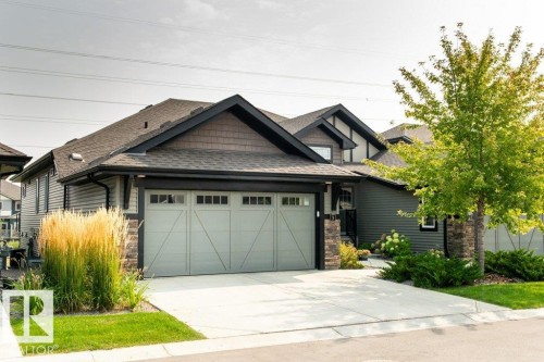 The property features a dark gray exterior, a two-car garage with an overhead door, and a concrete driveway - 3 8050 Orchards Green, Edmonton, AB - Outdoor