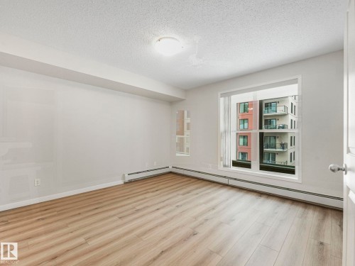This bright bedroom features new vinyl plank flooring, freshly-painted walls, and a large window providing views of nearby buildings - 515 10311 111 Street, Edmonton, AB - Indoor Photo Showing Other Room