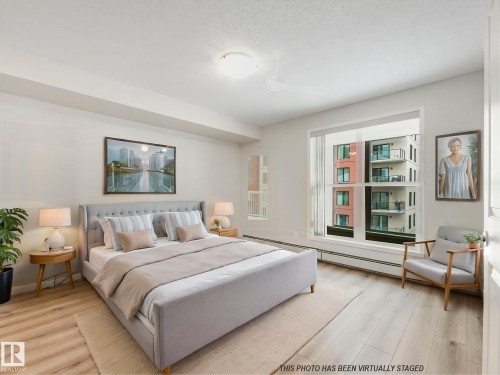 This bright bedroom features new vinyl plank flooring, freshly-painted walls, and a large west-facing window.  This photo includes virtual staging. - 515 10311 111 Street, Edmonton, AB - Indoor Photo Showing Bedroom