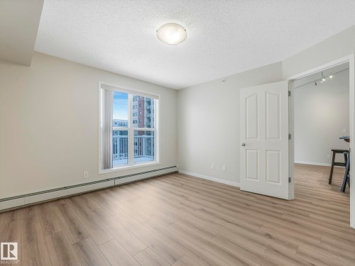 This bright room features a window with a view of other buildings, light-toned walls, and wood-style flooring - 515 10311 111 Street, Edmonton, AB - Indoor Photo Showing Other Room