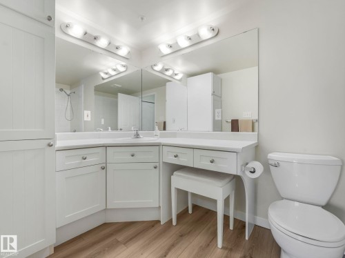 Bathroom featuring a white vanity with integrated sink, large mirrors, overhead lighting, and wood-style flooring - 515 10311 111 Street, Edmonton, AB - Indoor Photo Showing Bathroom