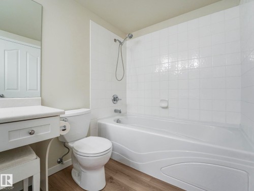 The bathroom features a white bathtub with a shower, a toilet, and a vanity with a mirror above it - 515 10311 111 Street, Edmonton, AB - Indoor Photo Showing Bathroom