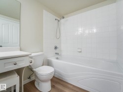 The bathroom features a white bathtub with a shower, a toilet, and a vanity with a mirror above it - 