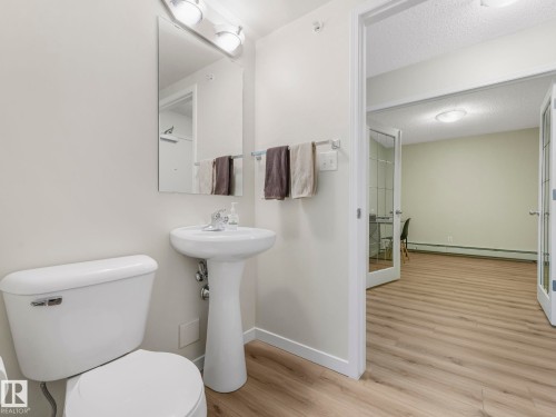 Bathroom featuring a white pedestal sink, a toilet, and a mirror with overhead lighting - 515 10311 111 Street, Edmonton, AB - Indoor Photo Showing Bathroom