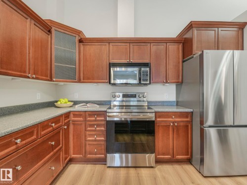 Well-appointed kitchen featuring wood cabinetry, stainless steel appliances, and ample counter space with a speckled finish - 515 10311 111 Street, Edmonton, AB - Indoor Photo Showing Kitchen
