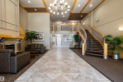Grand lobby featuring a curved staircase with wooden banisters, a tile floor, and a decorative chandelier - 515 10311 111 Street, Edmonton, AB - Indoor Photo Showing Other Room