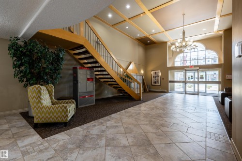 The property features a spacious lobby with a grand wooden staircase, tiled flooring, and an elegant chandelier - 515 10311 111 Street, Edmonton, AB - Indoor Photo Showing Other Room